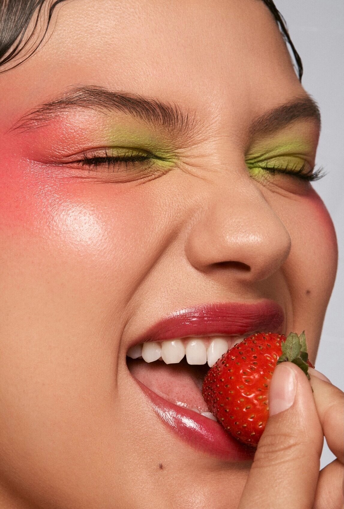 Pessoa com sombra colorida nos olhos desfrutando de um morango. Maquiagem vibrante e lábios brilhantes.  produtos com cheiro de frutas.