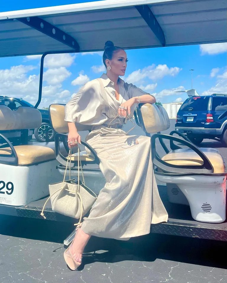 Mulher elegante sentada em um carrinho de golfe, com vestido brilhoso e bolsa combinando. Sapato polêmico de 2025 completa o visual.