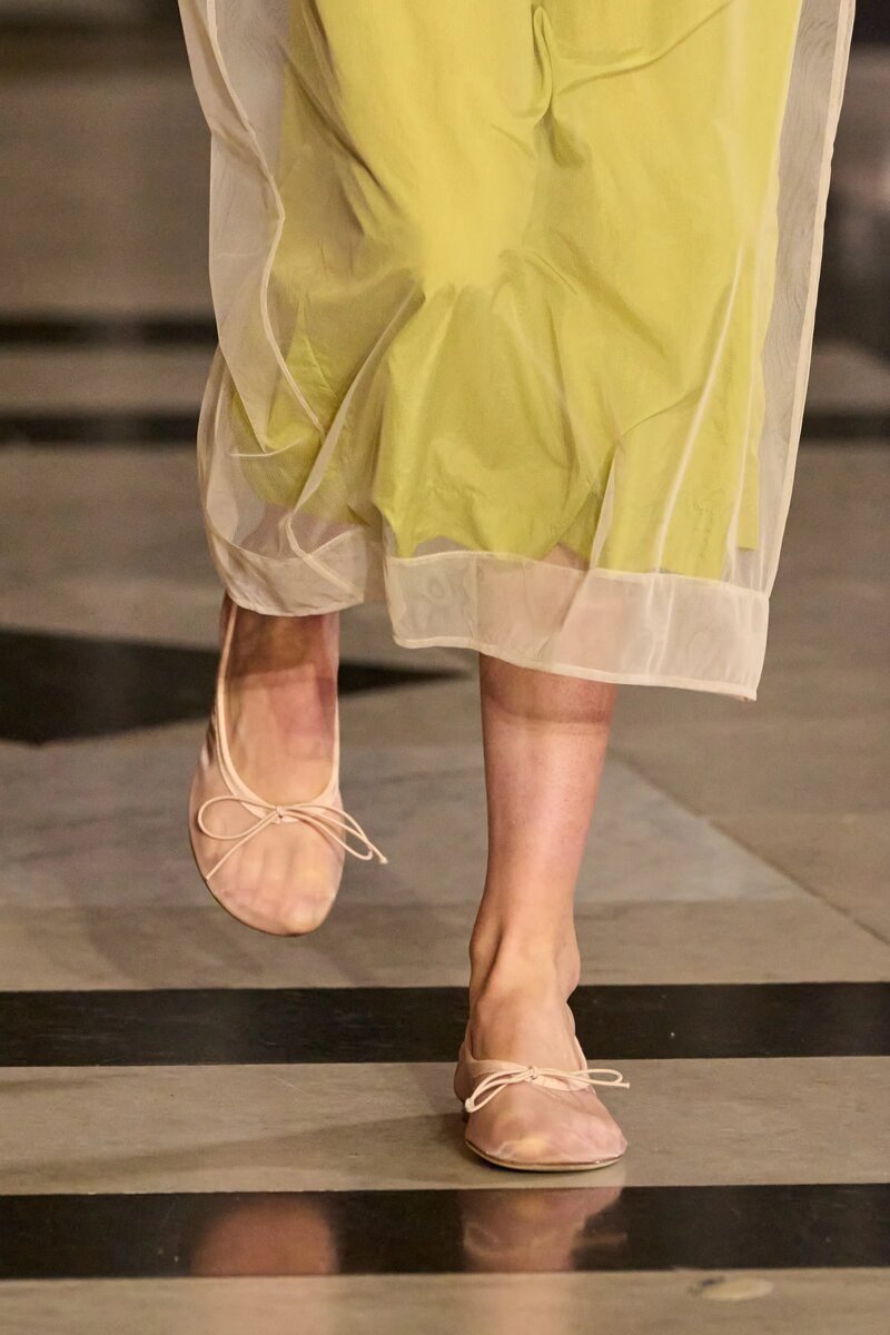 Modelo calçando sapatos transparentes e vestido amarelo pastel, destaque da moda como sapato polêmico de 2025.