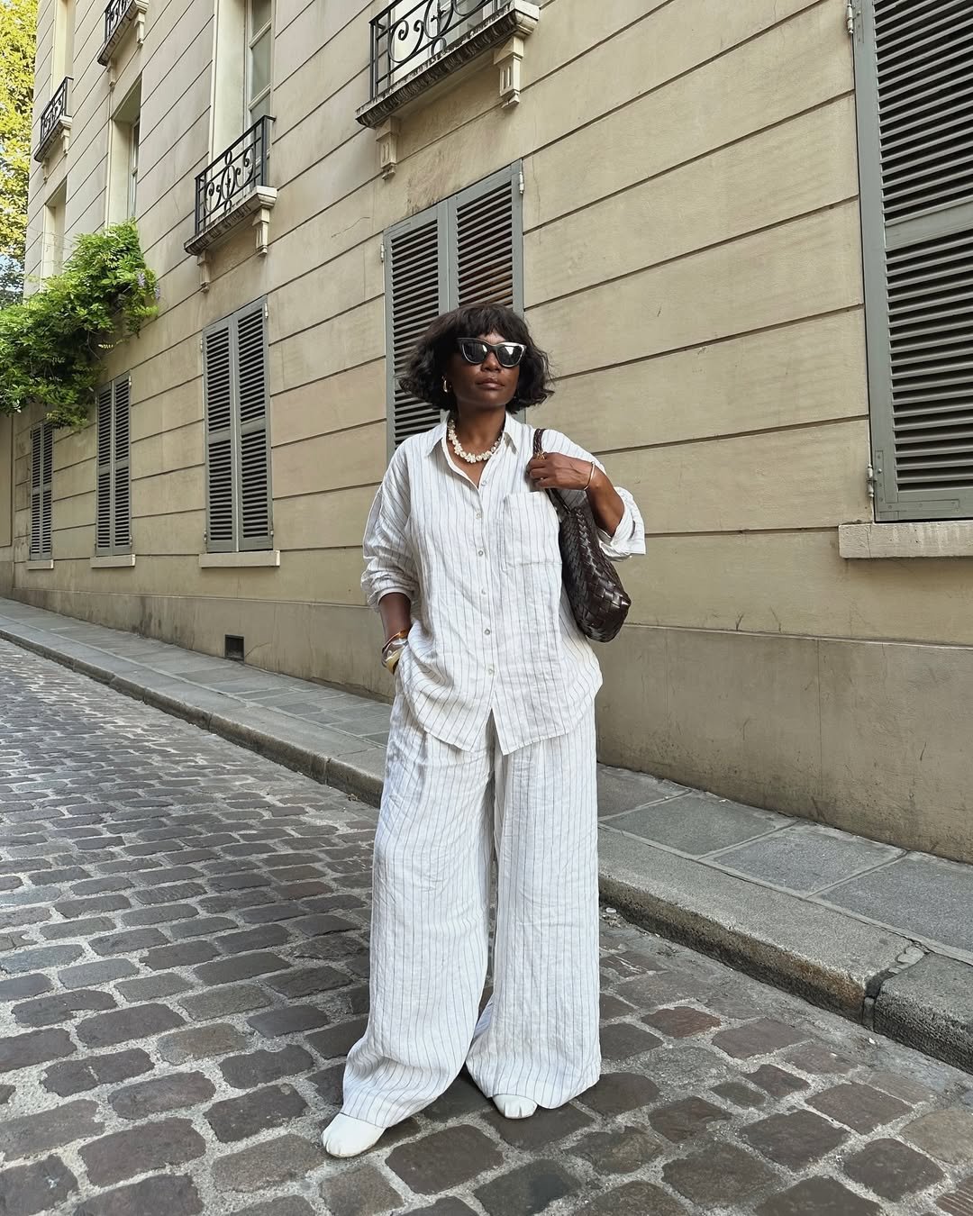 Pessoa com roupa listrada branca e sapatos de trabalho confortáveis, parada em uma rua de paralelepípedos.