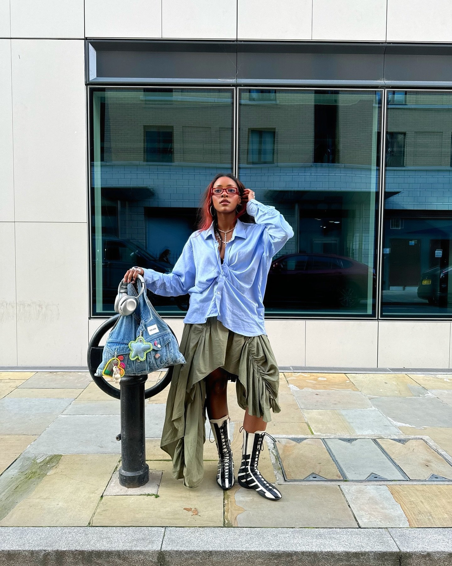 Pessoa com camisa azul e saia assimétrica, carregando uma bolsa. Usa botas pretas e brancas.