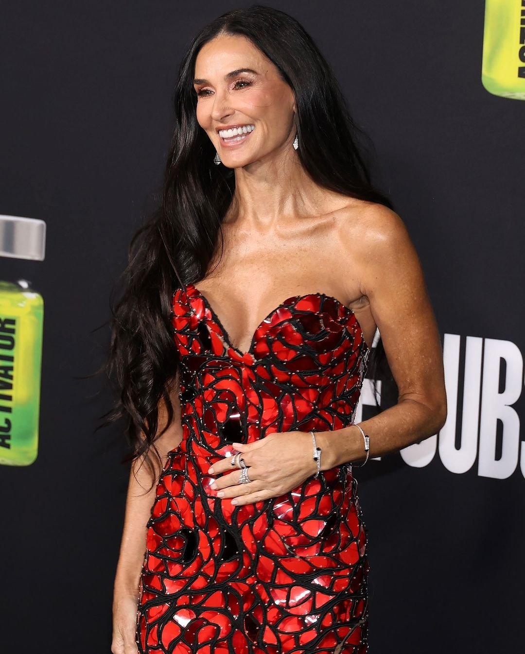 Mulher sorrindo, cabelo longo e solto, vestido vermelho com detalhes pretos. Olhos voltados para o lado, tendência em cortes de cabelo em 2025.