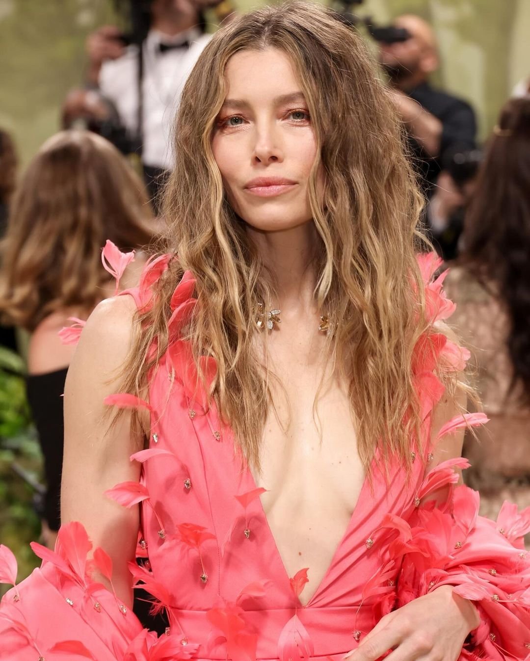 Cabelo ondulado solto e vestido rosa vibrante com pétalas, destacando tendência de cortes de cabelo em 2025.