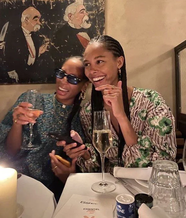 Duas mulheres sorridentes em um restaurante, com taças de espumante, sob decoração peculiar.