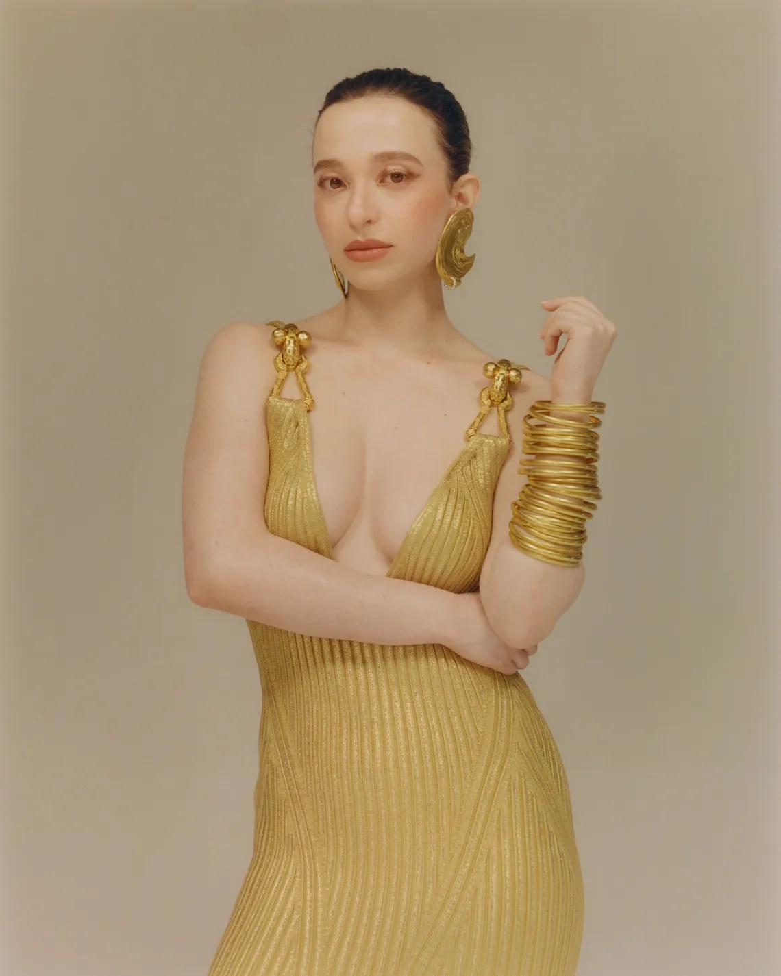 Mikey Madison com vestido dourado e acessórios, em pose elegante.