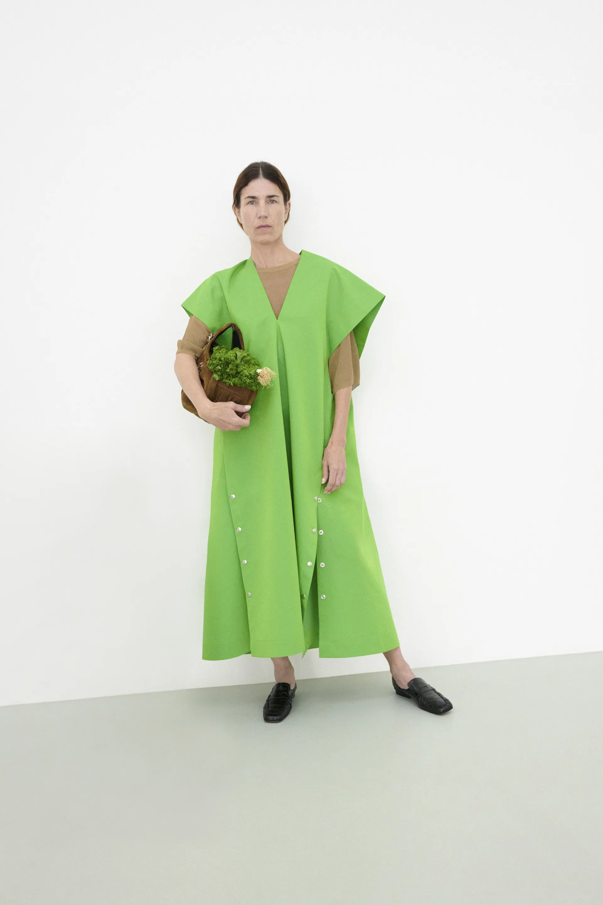 Vestido verde vibrante usado por pessoa segurando cesta com vegetais, evocando cores do verão 2025.