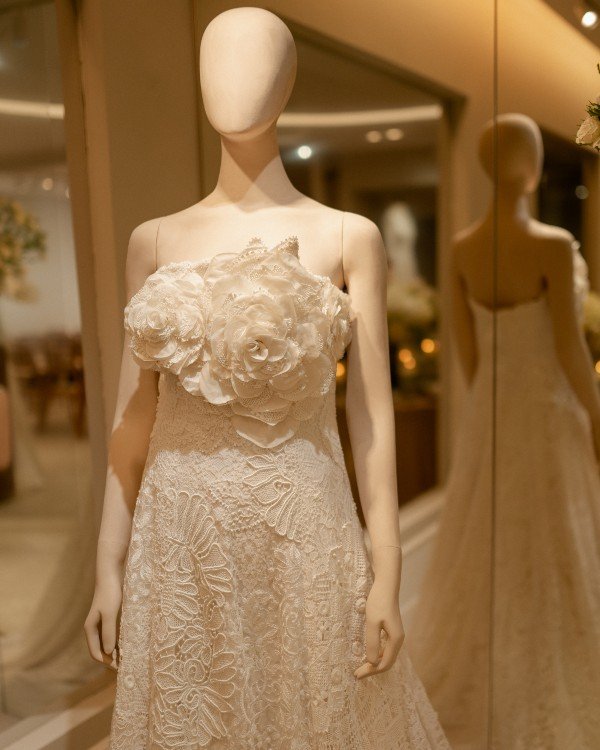 Vestido de noiva com flores em relevo no busto em uma vitrine de loja para noivas.