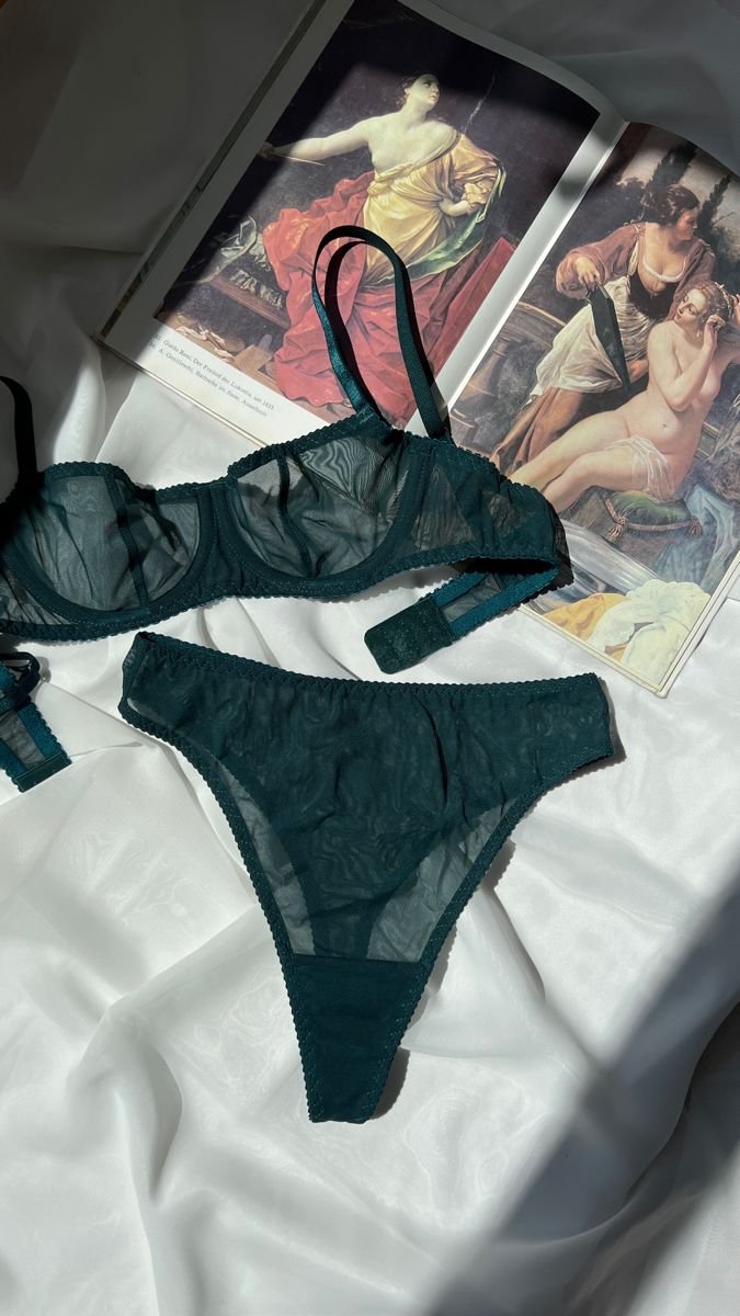 Lingerie verde-escuro sobre tecido branco com revistas ao fundo. Calcinha de ano novo