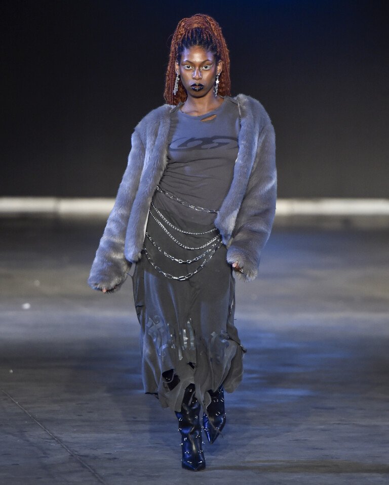 Desfile com modelo vestindo casaco de pelúcia e vestido preto com correntes, na Casa de Criadores 55.