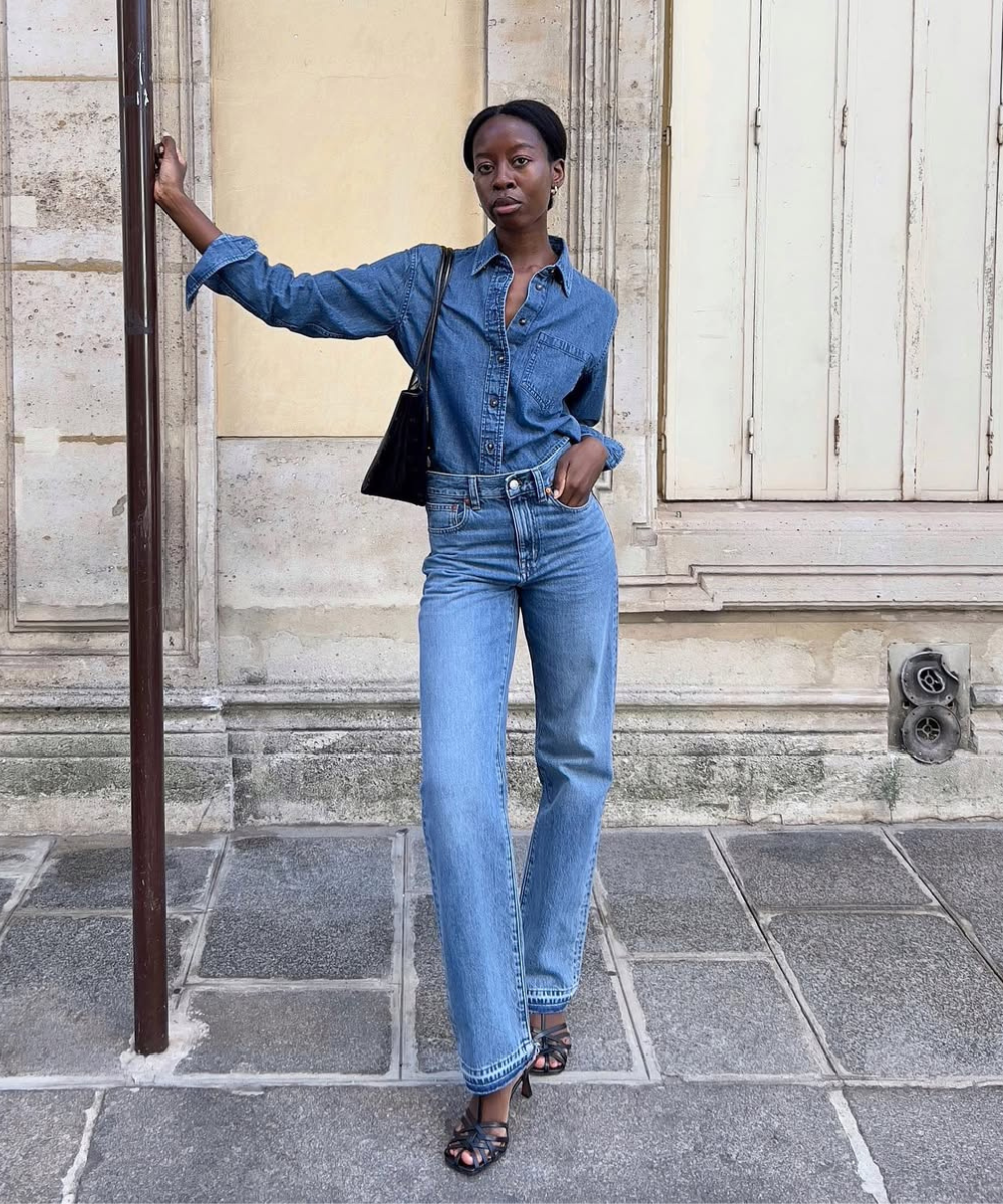 Pessoa usando conjunto jeans e bolsa preta, de pé na calçada. Mostra como usar bolsa preta com look jeans.