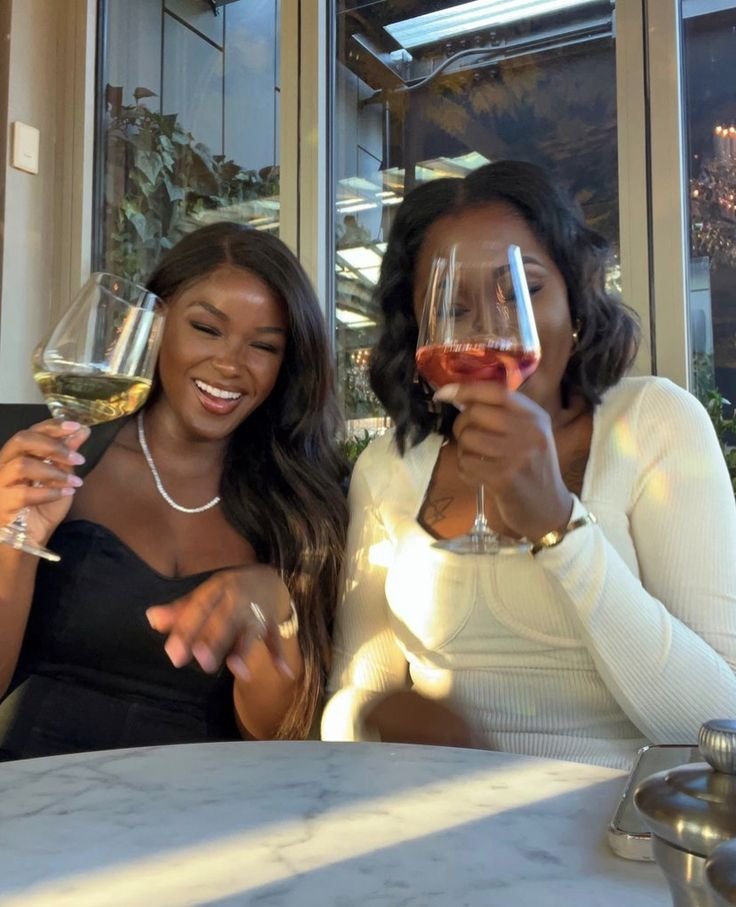 Duas mulheres sorridentes brindando com taças de vinho, aproveitando boa companhias em um ambiente elegante.