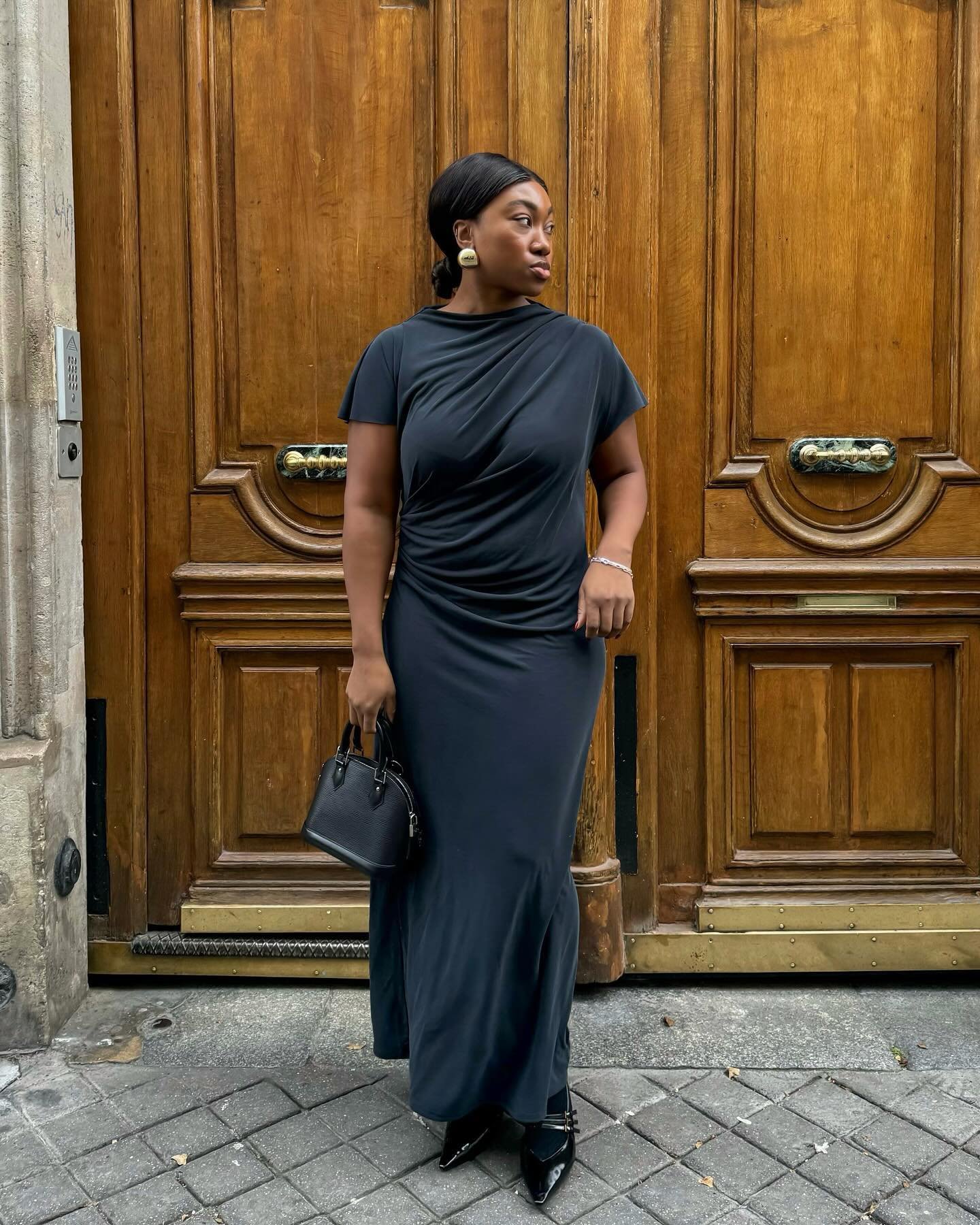 Vestido preto clássico em contraste com porta de madeira, destacando elegância e tendências das cores da moda.