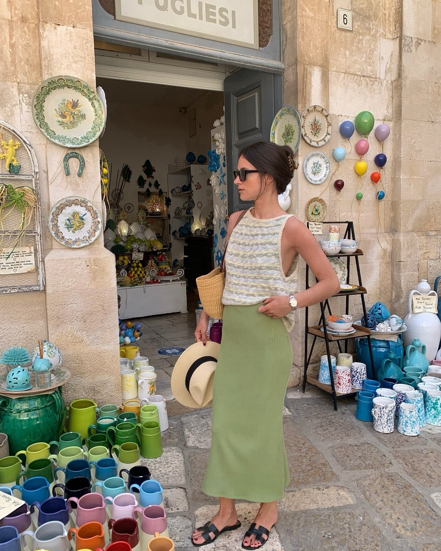 Mulher com saia verde e blusa listrada em loja de cerâmica colorida, destacando tons da moda.