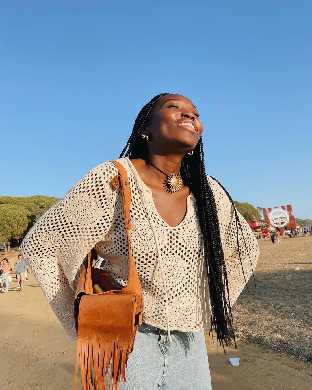 Moça sorrindo ao ar livre com blusa leve e bolsa de franjas. Não foi possível usar 