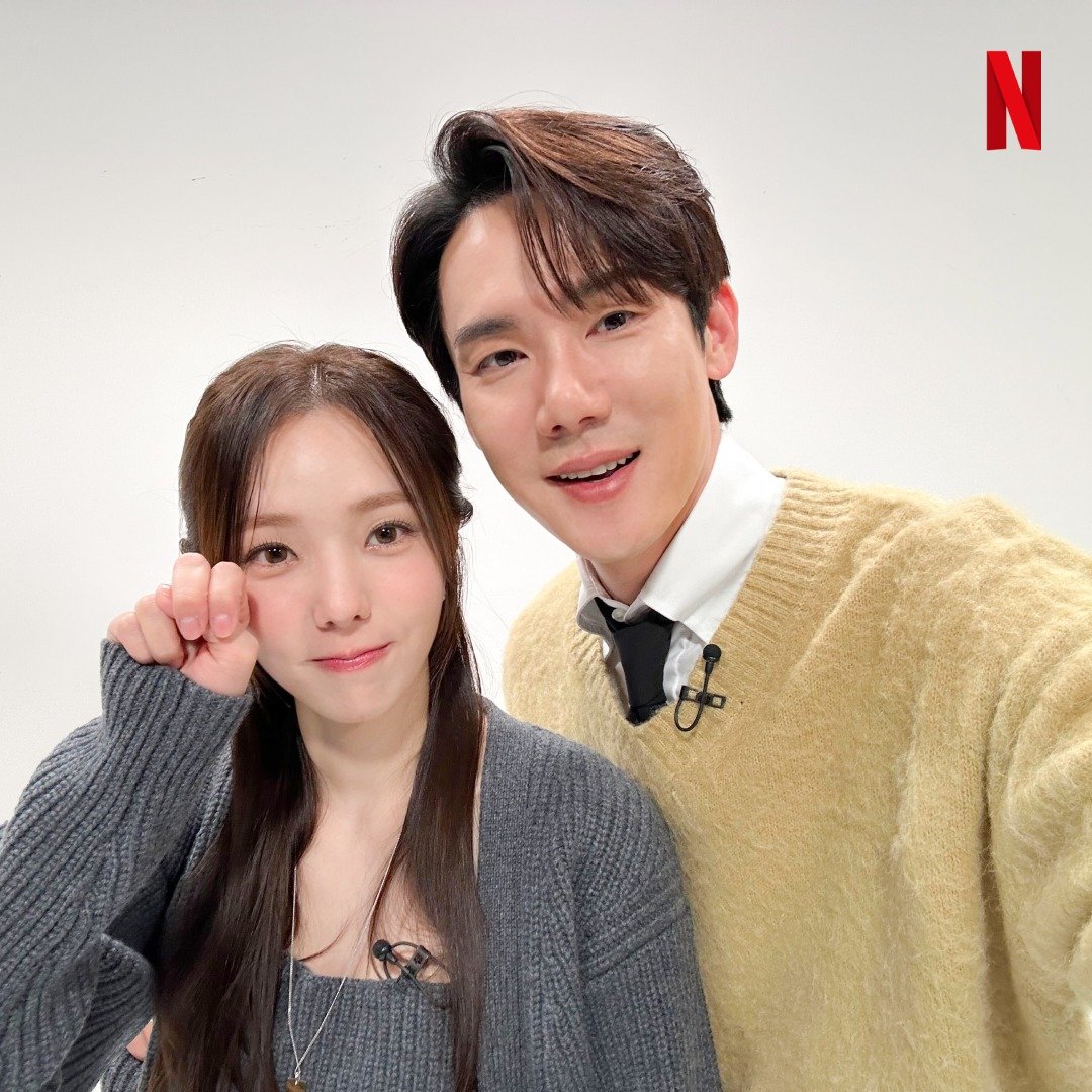 Casal sorrindo juntos em estúdio, vestindo roupas casuais. Elenco de um dos doramas da Netflix.