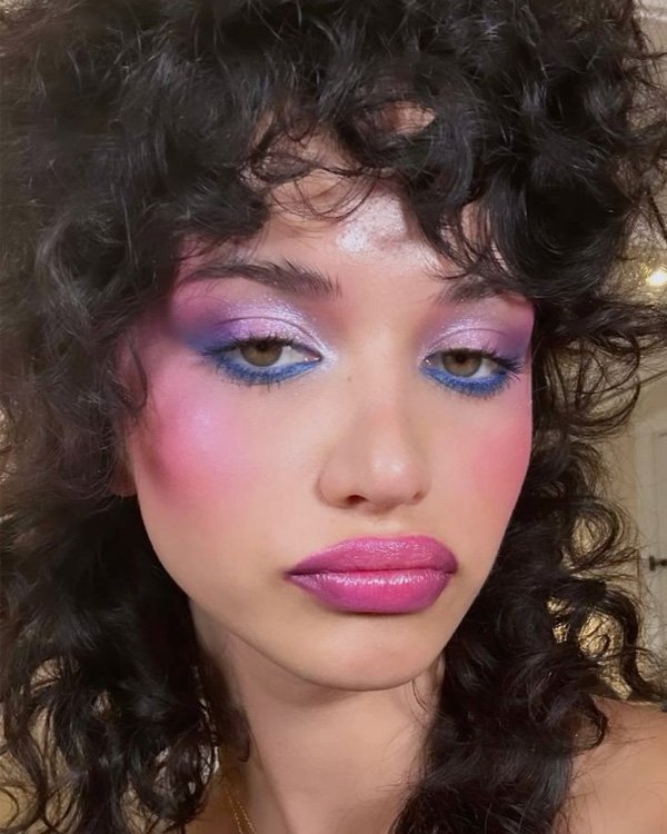 Maquiagem ousada com sombras rosa e azul e batom brilhante. Estilo reflete tendências de beleza de 2024.