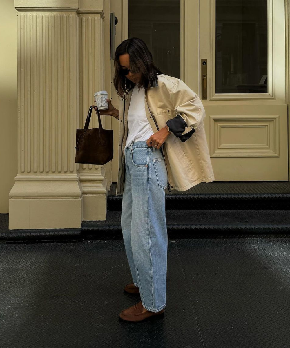 Pessoa com casaco beige, calça jeans, segurando café e bolsa. Usa mocassins, compondo looks estilosos com mocassim.