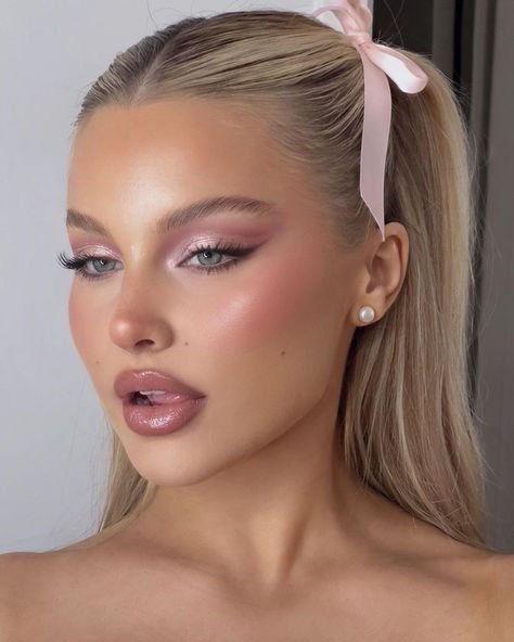 Mulher com maquiagem de ano novo: sombra rosada, blush suave e lábios nude, cabelo preso com laço rosa.