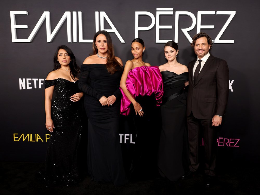 Grupo elegante em evento de gala, usando roupas sofisticadas inspiradas no mercado de luxo, em frente a um cartaz.