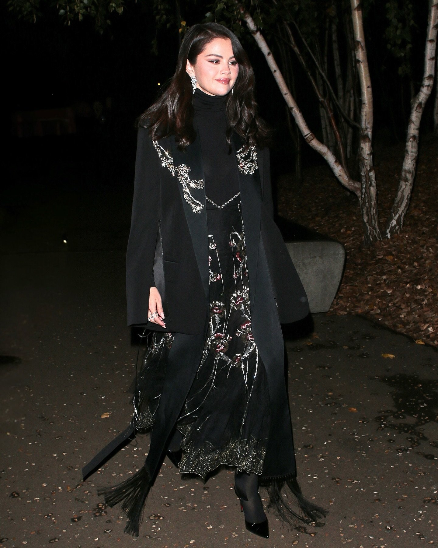 Mulher em vestido preto elegante com bordados, estilo reminiscente da moda dos anos 20, caminando em uma rua à noite.