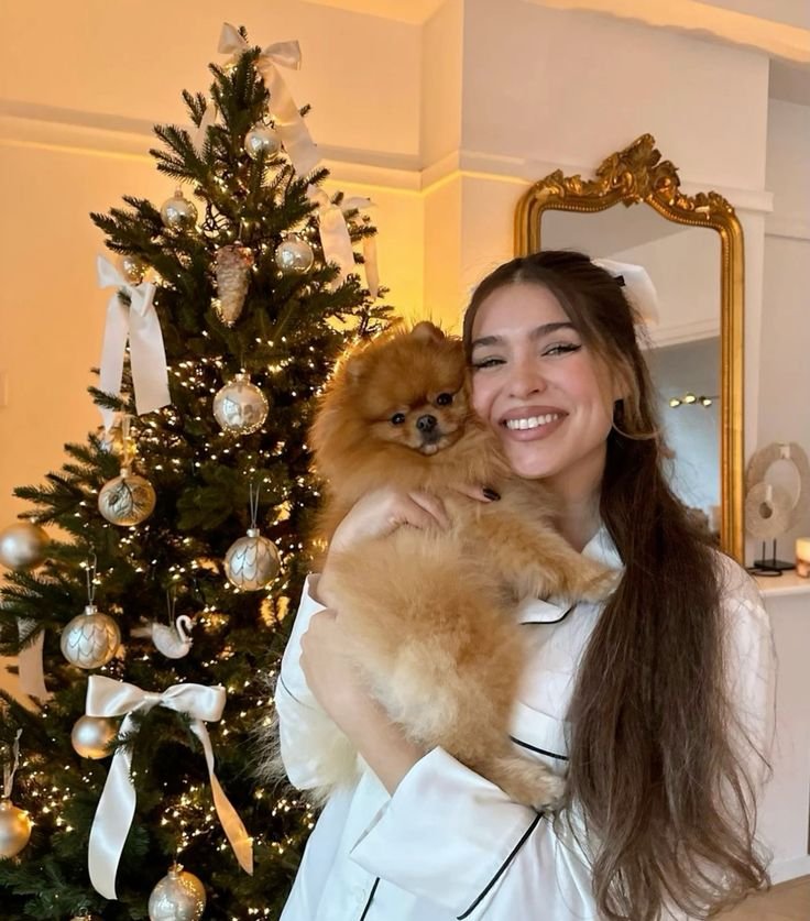 Jovem sorridente com cachorro ao lado de árvore de Natal iluminada, transmitindo boas energias no Natal.