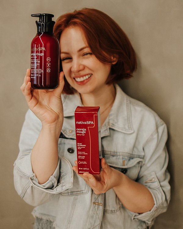 Mulher sorrindo segura produtos nativaSPA cereja rouge, ideais para Kit de final de ano.