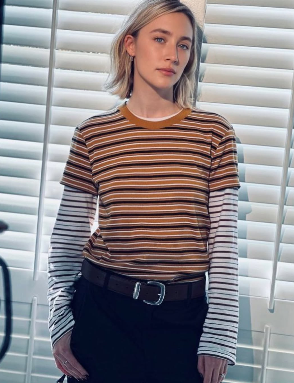 Saoirse Ronan posando em frente a persianas, usando uma camiseta listrada.