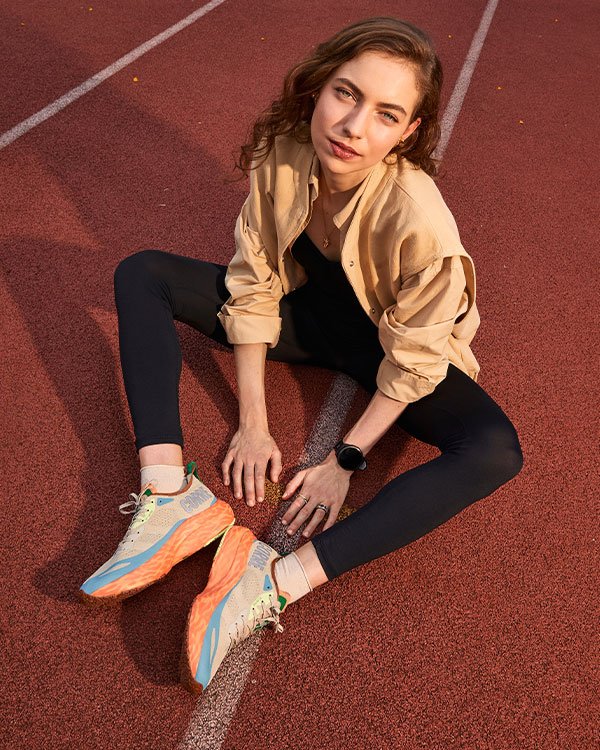 Mulher sentada em pista de corrida, usando tênis coloridos Olympikus e Authentic Feet.