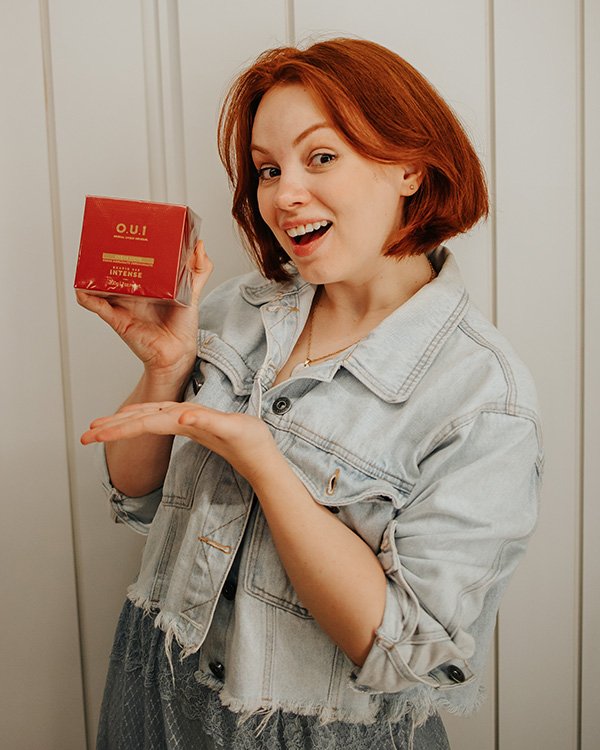 Pessoa segurando uma caixa vermelha de perfume, sorrindo. Possível sugestão de presente em um kit de final de ano.