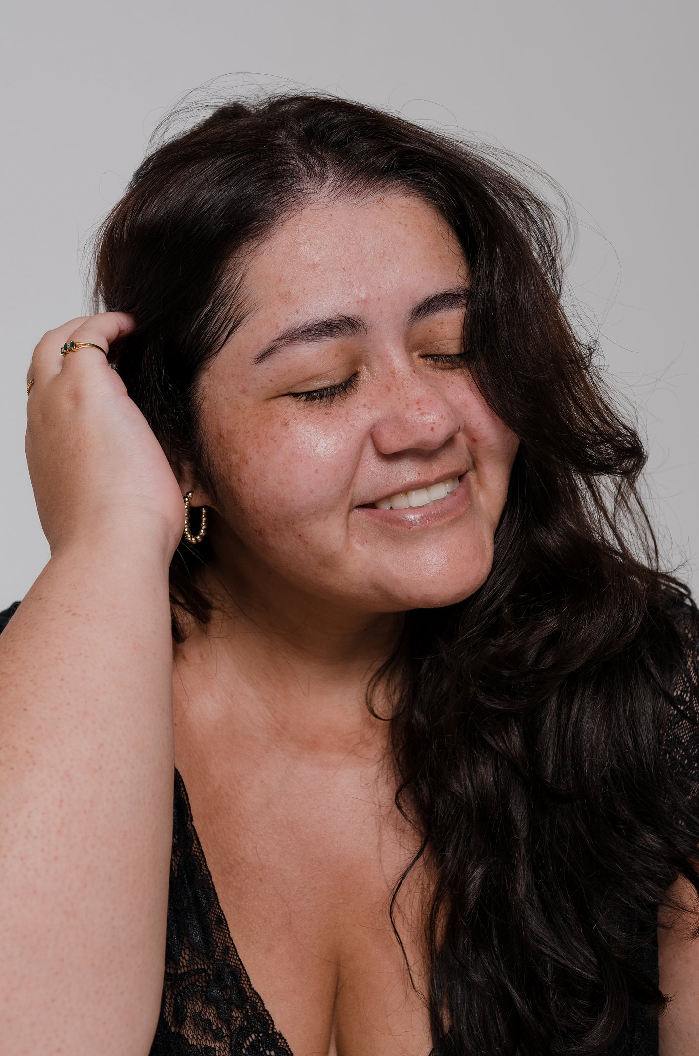 Mulher sorrindo com pele naturalmente manchada, cabelo solto e olhos fechados.