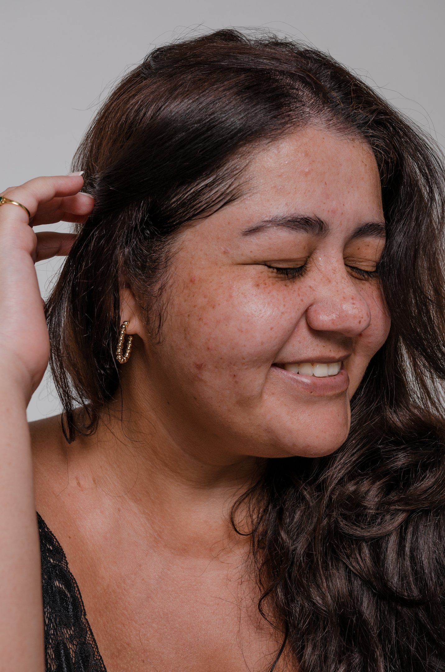 Mulher sorrindo com a pele com manchas morena natural usando brinco dourado.