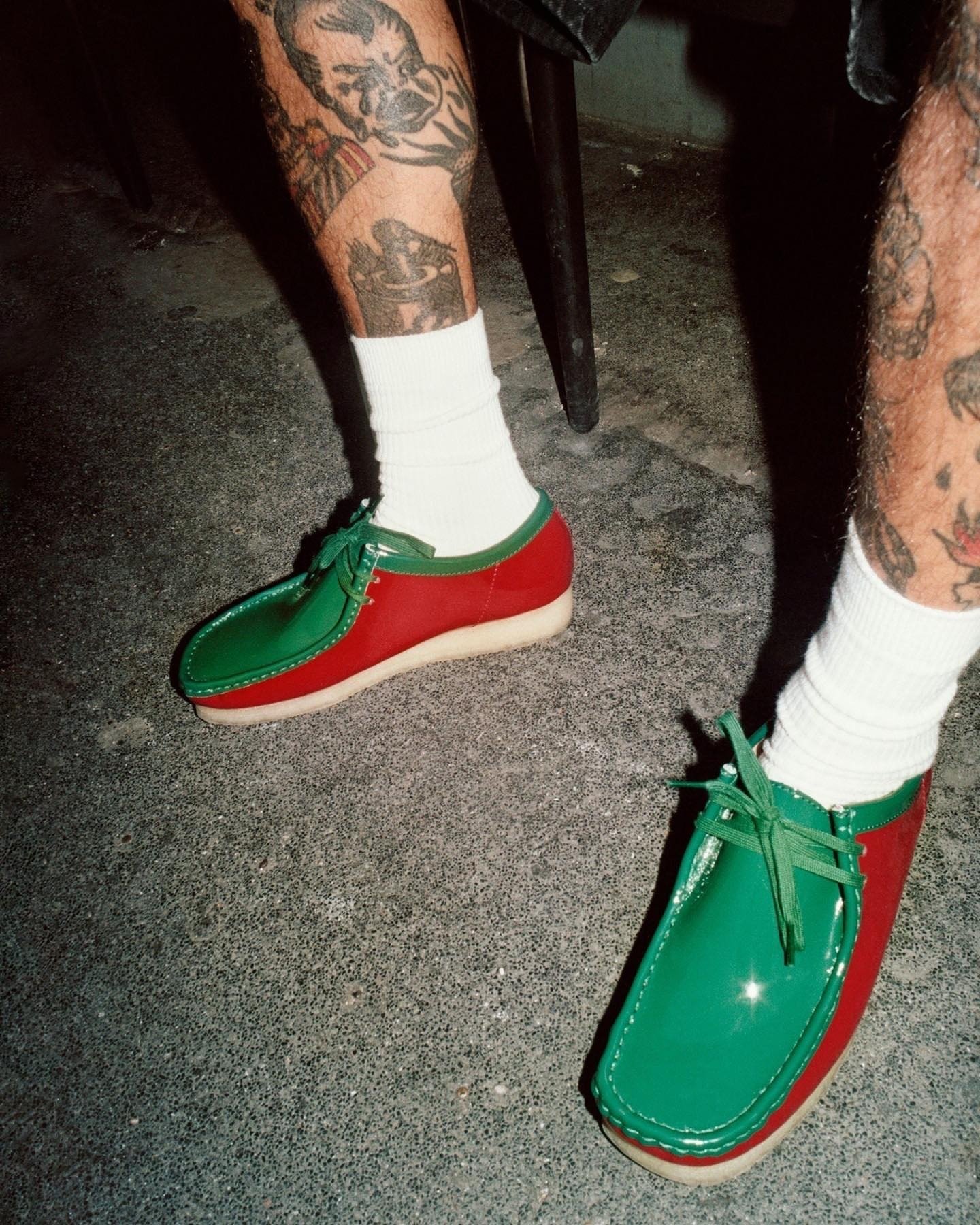 Sapatos estilo wallabees em cores vibrantes, verde e vermelho, usados com meias brancas. Pernas tatuadas visíveis.