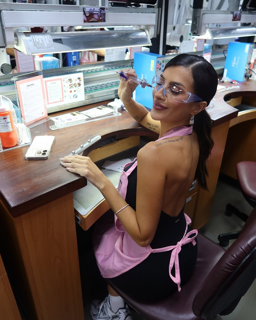 Mulher em laboratório, com óculos de proteção e avental rosa, sentada em bancada de trabalho. Tailândia mencionada.