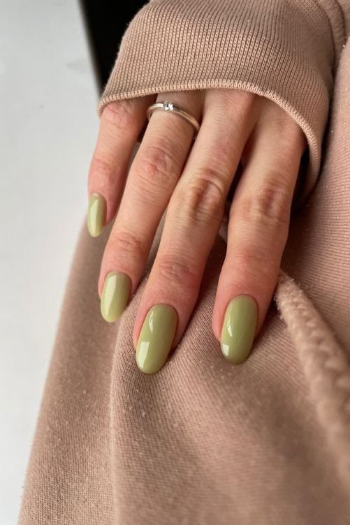 Mão feminina com unhas pintadas de verde claro, tendência de unhas para ano novo 2025.