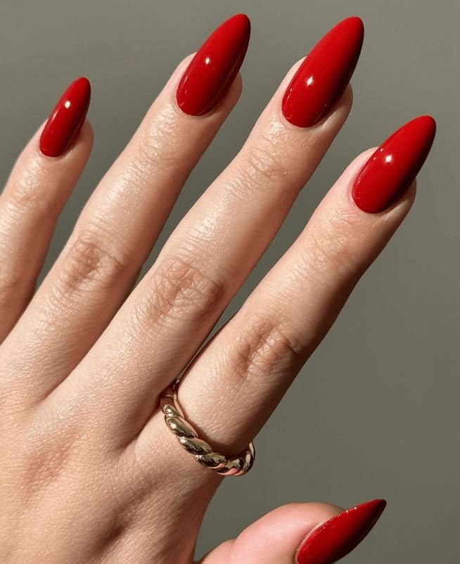 Unhas para Ano Novo 2025 vermelhas brilhantes e alongadas, com anel dourado elegante.