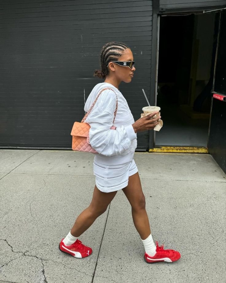 Pessoa caminha na rua com look casual, usando tênis vermelhos. Carrega bolsa laranja e bebida. Tênis perfeito para cada ocasião.