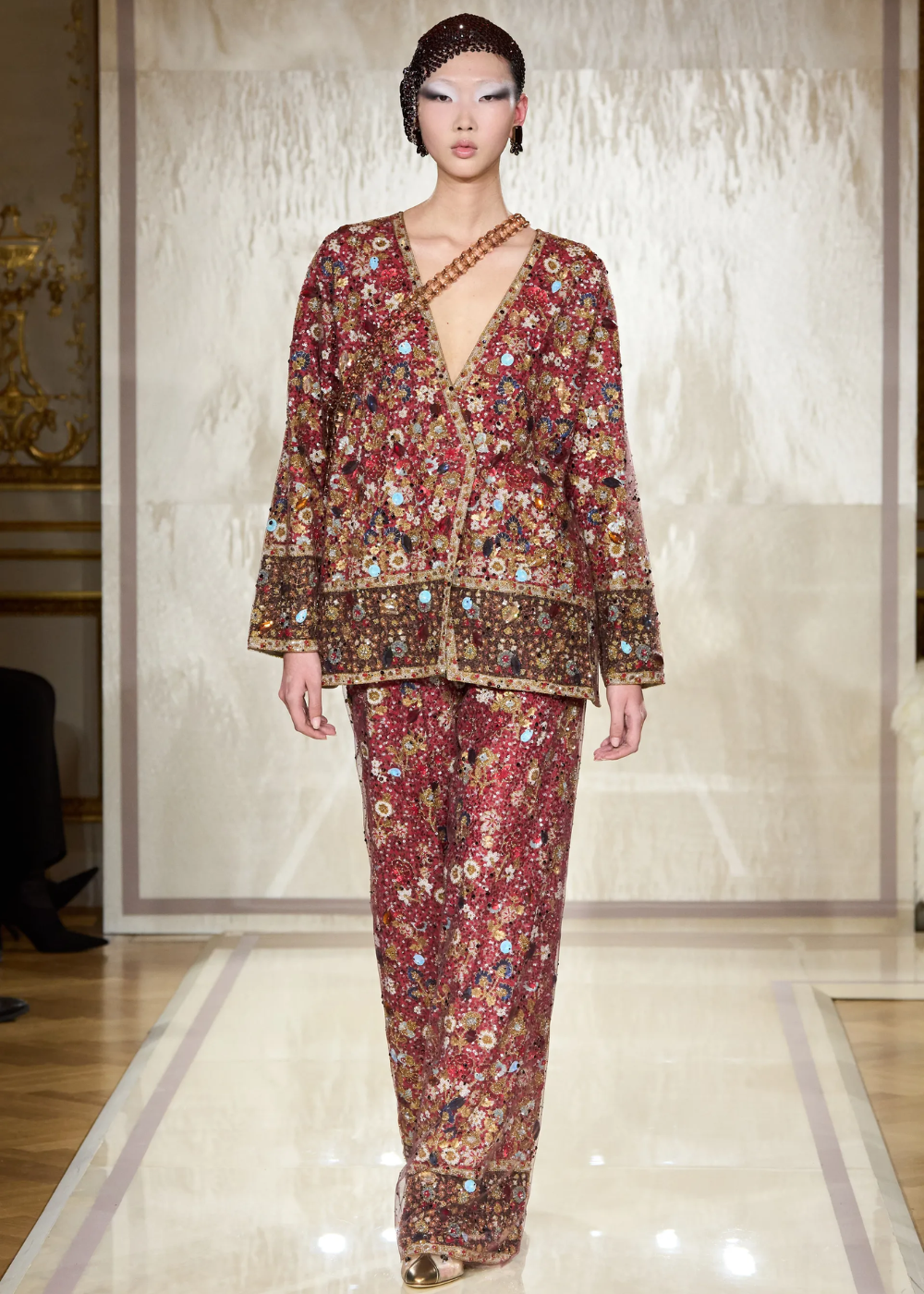 Modelo com traje floral bordado vermelho e dourado na passarela da Semana de Alta-Costura 2025.