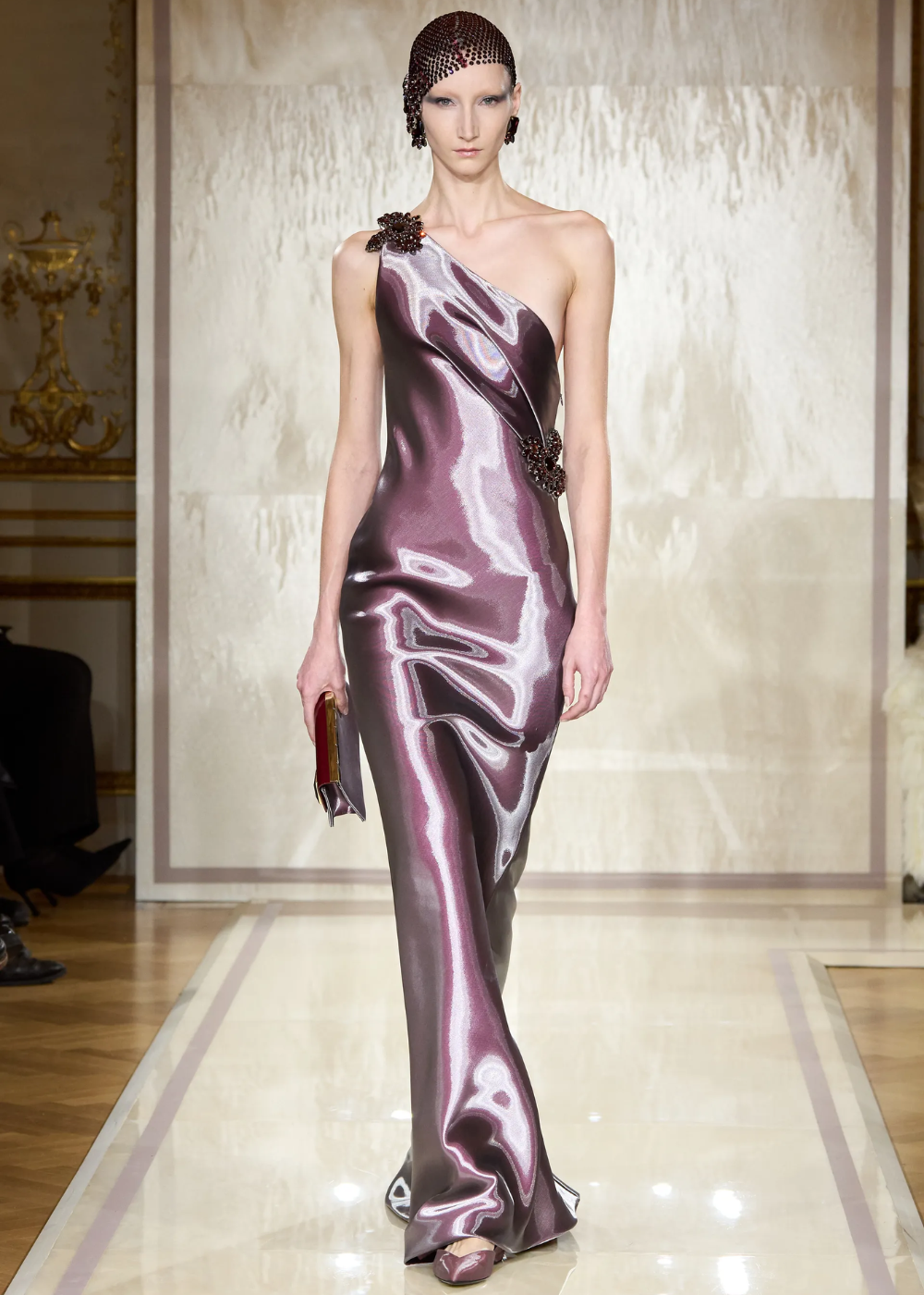 Modelo desfila em vestido metálico de um ombro só na Semana de Alta-Costura 2025, com detalhe floral.