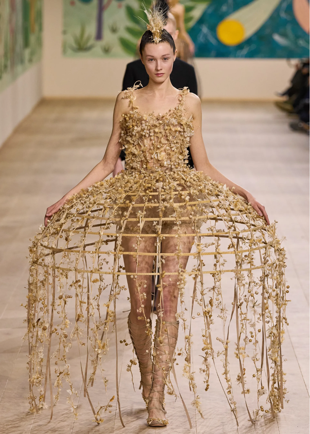 Desfile de moda com modelo vestindo vestido dourado intrincado e estruturado na Semana de Alta-Costura 2025.