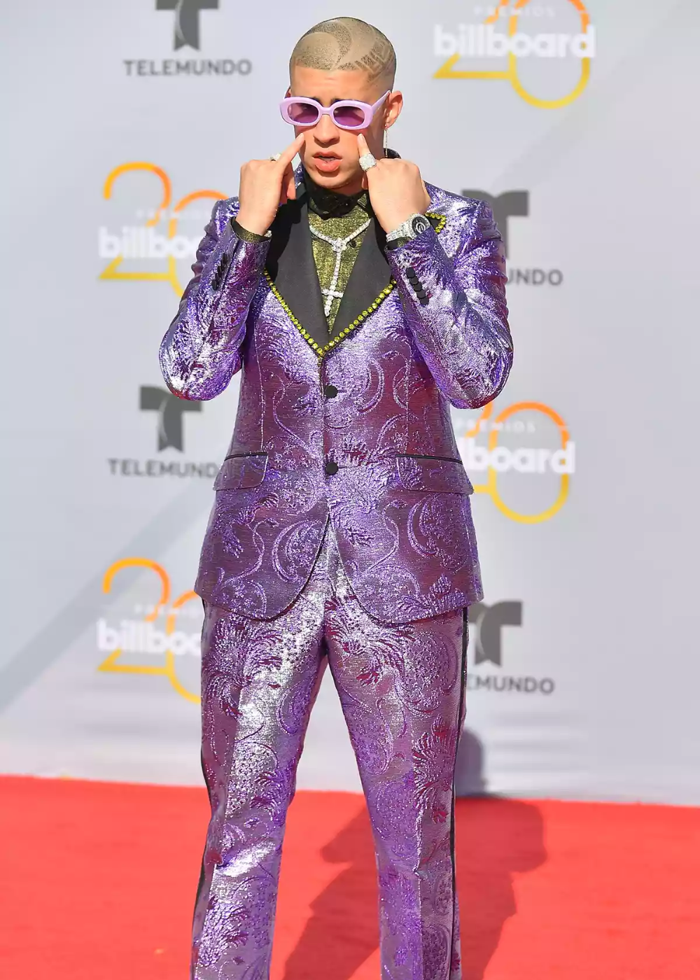 Homem de terno roxo brilhante e óculos escuros rosas posa no tapete vermelho de evento Billboard.