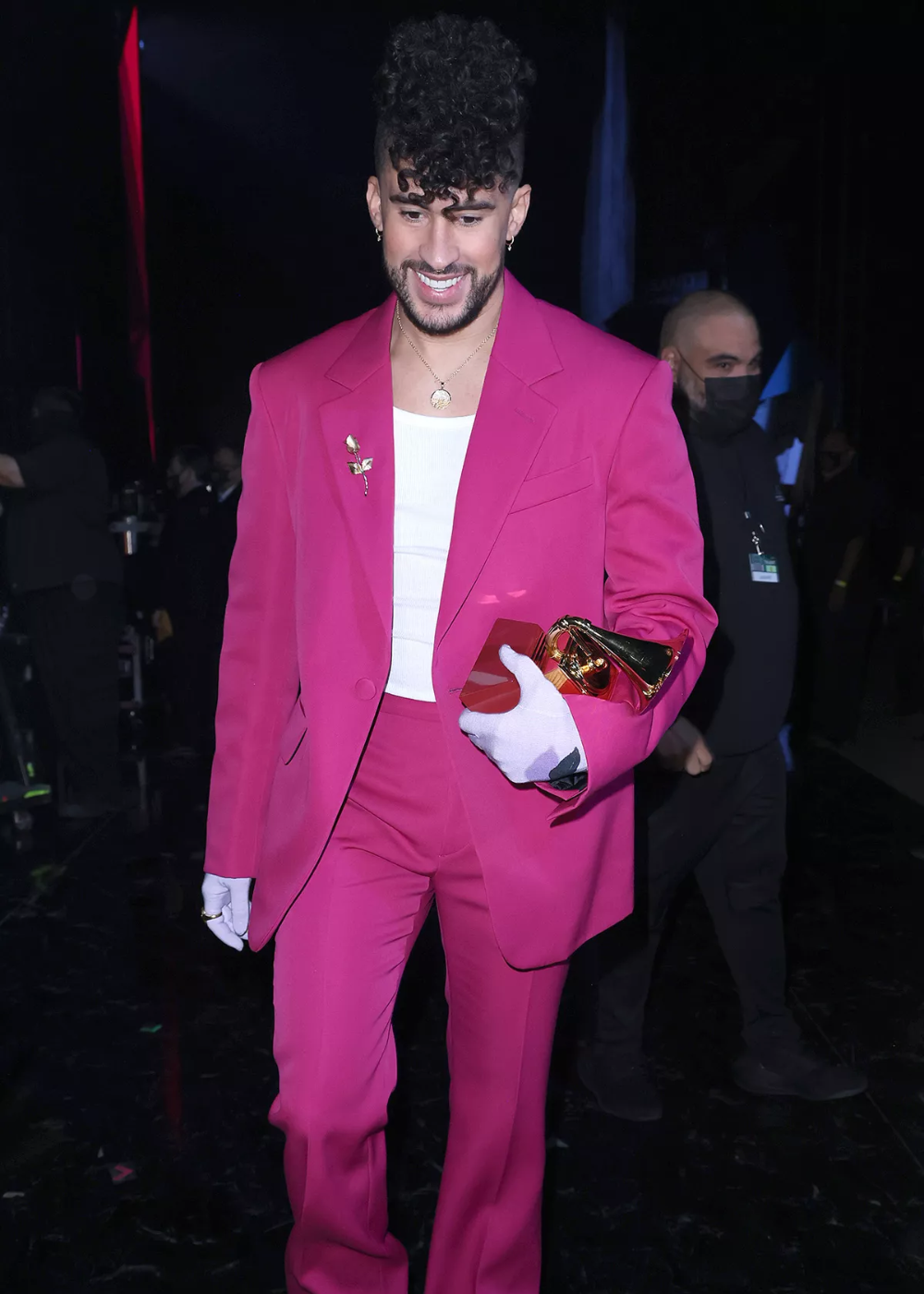 Pessoa sorrindo, usando terno rosa vibrante e segurando um Grammy. Bad Bunny esteve em um evento.