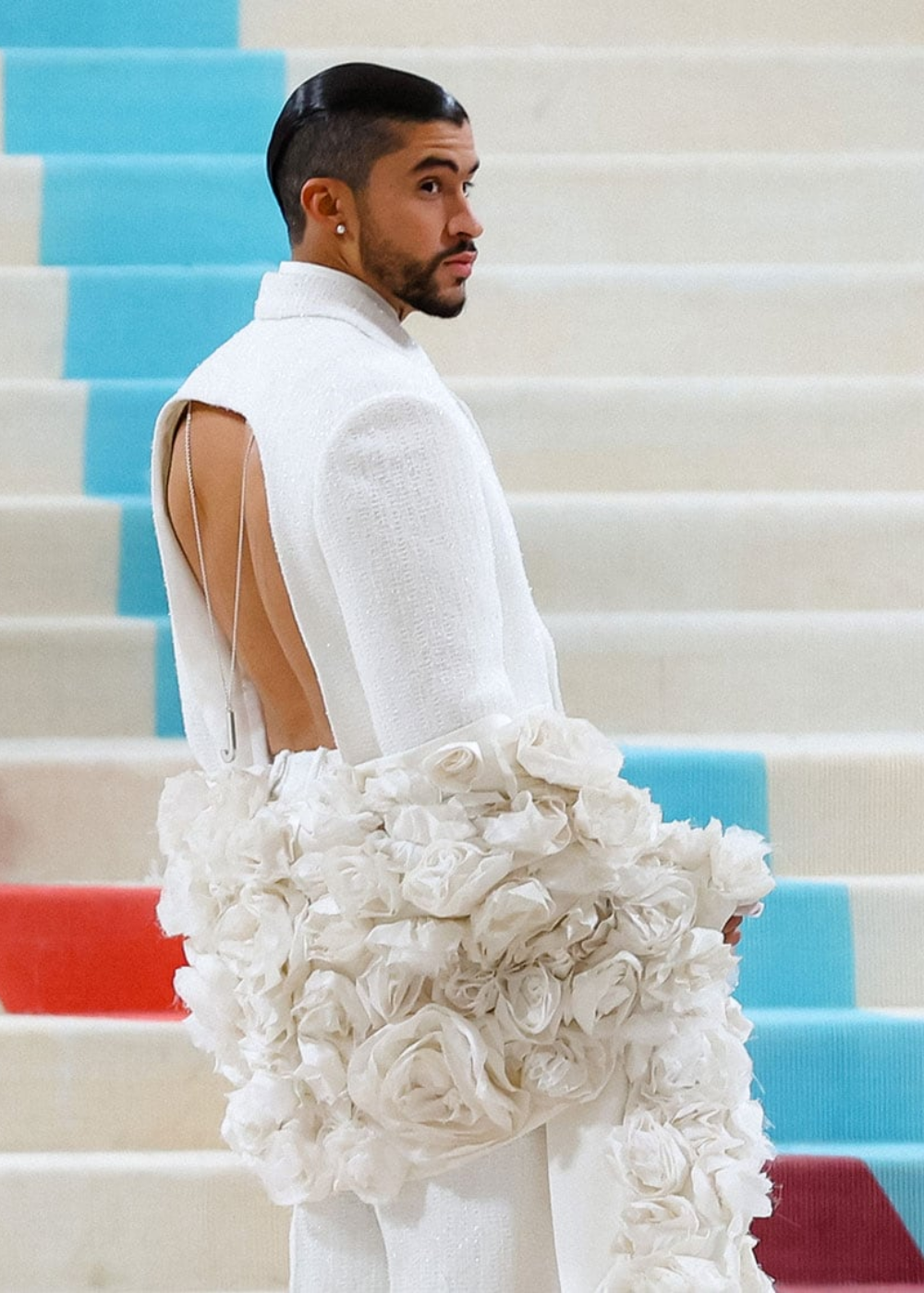 Um homem em traje branco elegante com detalhe de flores posa em escada colorida.