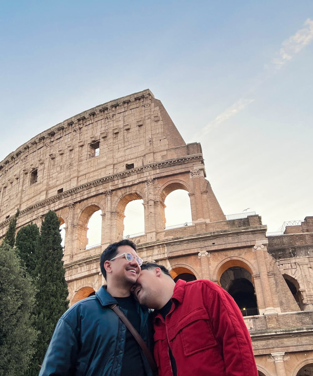 Coliseu ao fundo com duas pessoas sorrindo; cenário típico de viagem pela Europa.