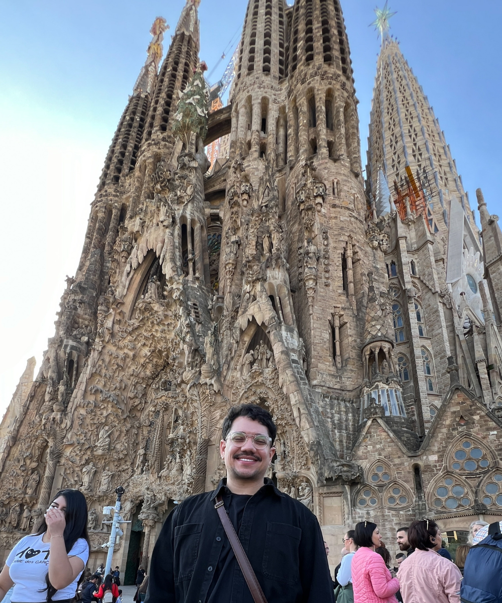 Homem sorrindo na frente da Sagrada Família em Barcelona, um destino popular ao viajar pela Europa.