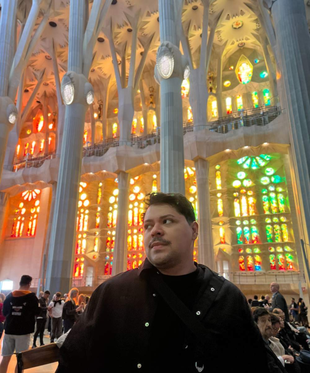 Homem em frente a vitrais coloridos da Sagrada Família, Barcelona. Uma das paradas ao viajar pela Europa.