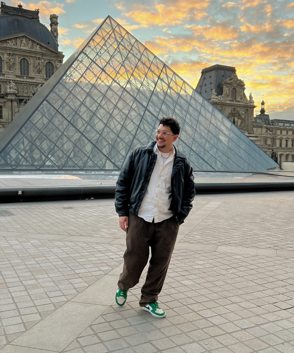 Pessoa sorridente ao lado da pirâmide do Louvre durante o pôr do sol. Perfeito para viajar pela Europa.