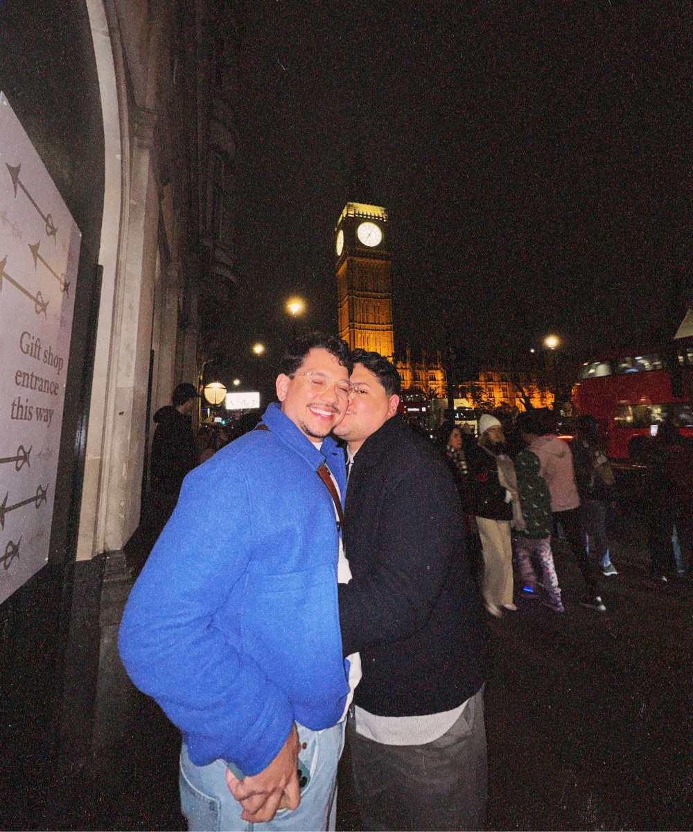 Duas pessoas sorrindo à noite em frente ao Big Ben iluminado, representação de 