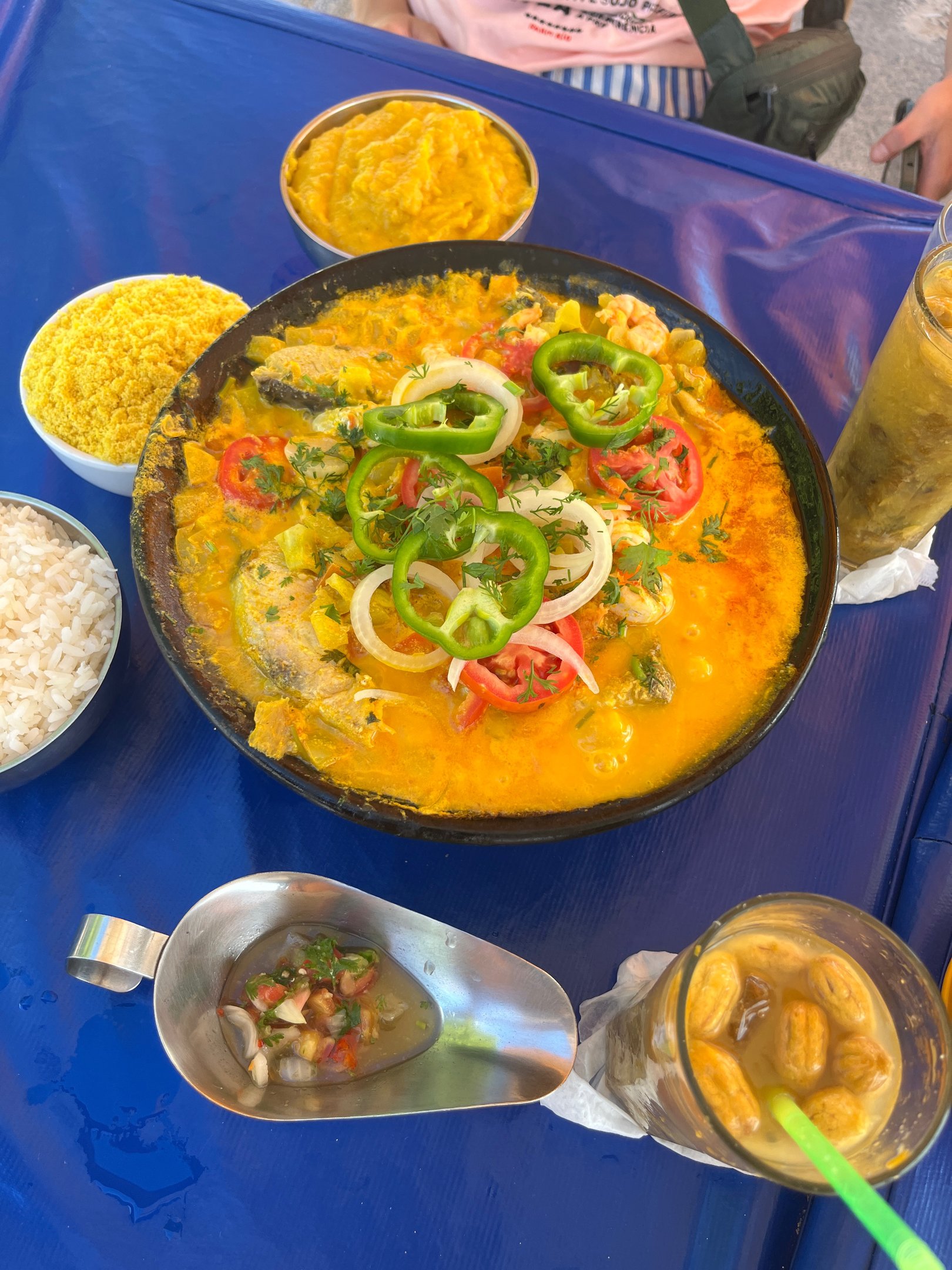 Prato de moqueca com peixe, arroz, farofa, pirão e molho acompanhados de um copo de bebida. sugerindo o que fazer em Salvador