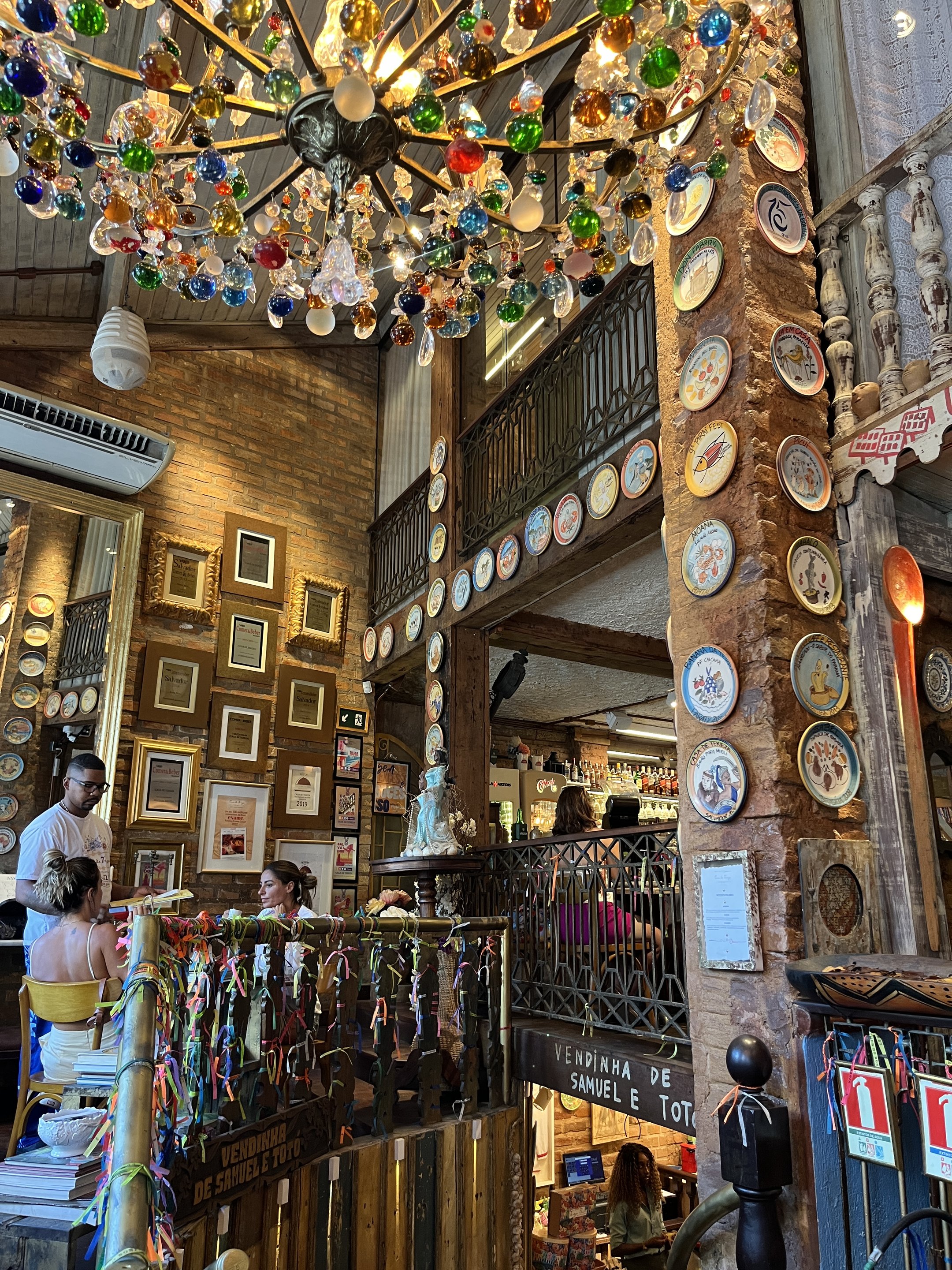 Restaurante em Salvador decorado com pratos de cerâmica, fitas coloridas e lustre adornado com vidros multicoloridos. sugerindo o que fazer em Salvador