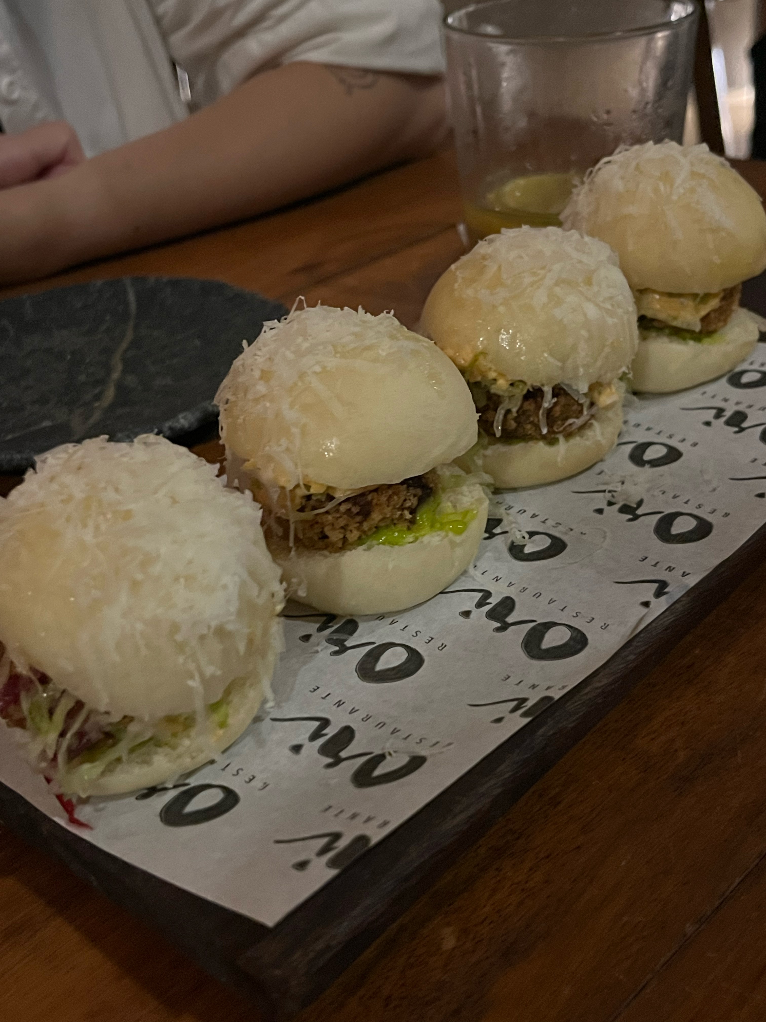 Deliciosos sliders com queijo ralado em cima, servidos sobre papel branco na tábua de madeira. sugerindo atividades gastronômicas para fazer em Salvador.